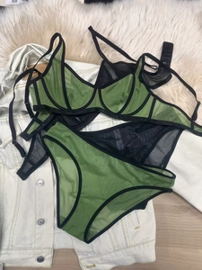 Detail of green mesh lingerie set with black trim and underwire on white fur background