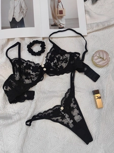 Flat lay of black floral lace lingerie set with bralette, thong, and scrunchie detail