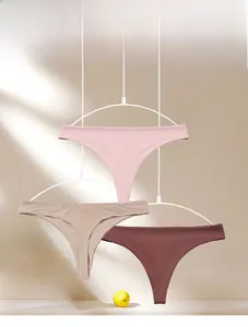 Three seamless thong panties in pink, nude and brown hanging against a soft window light