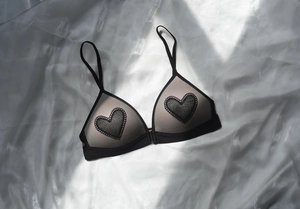 Detail of French triangle cup bra with black heart embroidery and lace on silk background