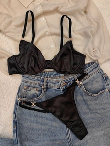 Flachbild von schwarzem Satin-Dessous-Set mit Strass-X-Schnallen auf Strick-Hintergrund