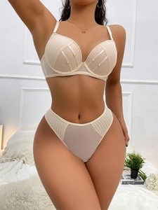 Dettaglio completo di lingerie beige in pizzo con mesh e anelli in metallo dorato lucido