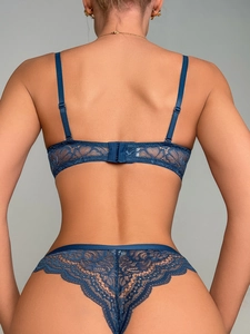 Detail of dark blue lace bra back straps and matching thong on model with grey background