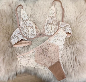 Flat lay of pale pink lace lingerie set with floral embroidery on white plush background
