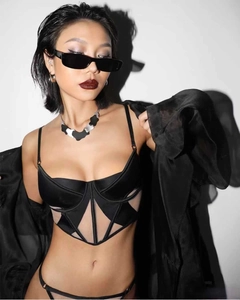 Dettaglio di un corsetto nero geometrico in mesh con pannelli di raso e cardigan