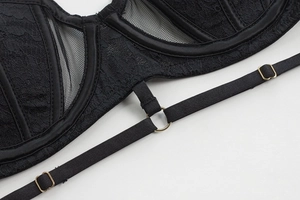 Macro detail of black lace bra featuring floral patterns and gold metal ring hardware