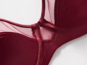 Close-up of dark red satin fabric and sheer mesh panels with fine stitching on a bra