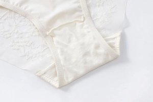Detailed close-up of cream satin panties with floral lace embroidery and sheer mesh texture