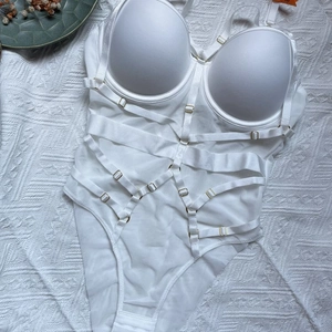 Detailed flat lay of white bodysuit featuring cross-strap design and gold metal buckles
