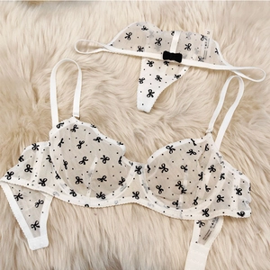 Détail d'un ensemble de lingerie en tulle blanc avec motifs nœuds noirs et bretelles