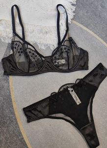 Flat lay of black lace bra and thong set with polka dot embroidery on gray texture
