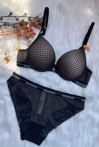 Flat lay of black mesh lingerie set with branded straps on a white plush rug