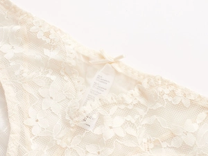 Détail de la broderie en dentelle florale et du nœud en satin sur culotte beige