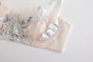 Detailed close-up of light pink lace bra featuring silver floral embroidery and mesh texture