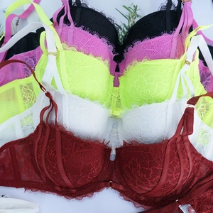 Dettaglio flat lay di completi intimi in pizzo cigliato in rosso vino, bianco, verde e nero