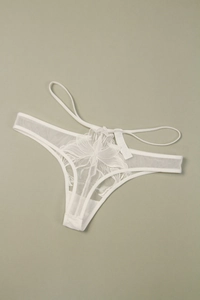 Détail d'un string en dentelle blanche transparente avec de délicates broderies florales