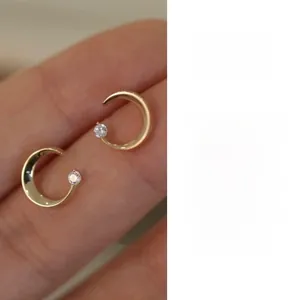 Macro shot of a 14K gold crescent moon stud earring with a sparkling white zircon stone