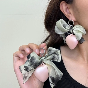 Detailed close-up of handmade silk bow earrings with a soft pink frosted heart pendant