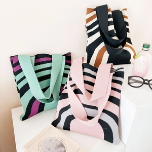 Knitted tote bag with colorful wavy stripes and wide shoulder straps on a display stand