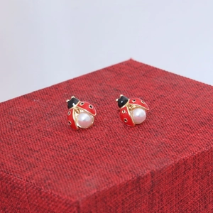 Gros plan détaillé de boucles d'oreilles coccinelle avec émail rouge et perles blanches