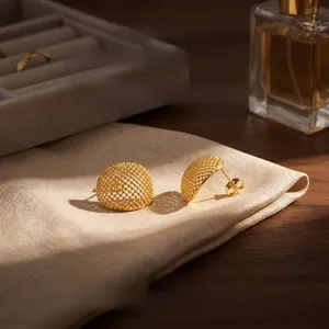 Detail of 18K gold plated hollow honeycomb dome earrings on a soft fabric texture