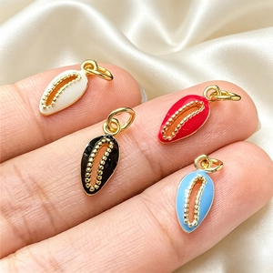 Golden shell charms with colorful enamel finish shown in hand on beige satin fabric