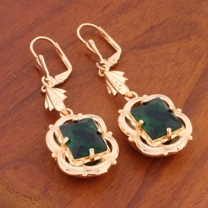 Golden drop earrings with rectangular emerald green crystal on a rustic wood background