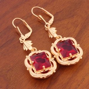 Detail view of golden earrings with red square-cut crystals on a wooden surface