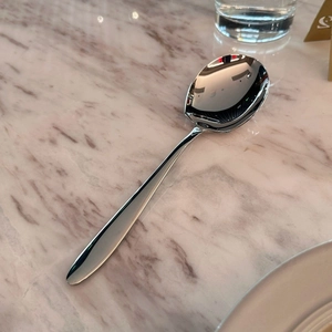 Macro detail of high-polish stainless steel serving spoon on marble tabletop