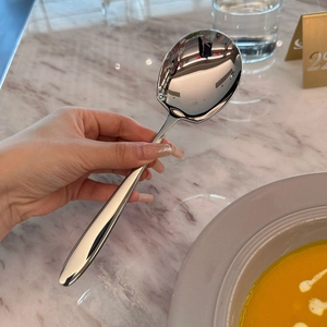 Polished stainless steel serving spoon with a thick long handle in a dining setting