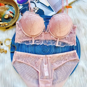 Flat lay of pink lace lingerie set with floral embroidery and size tag on a blue mat