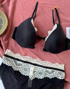 Detailed flat lay of black lace lingerie set with white embroidery on pink fabric background