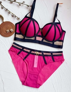 Détail d'un ensemble de lingerie fuchsia et noir avec pendentif G doré sur fond blanc