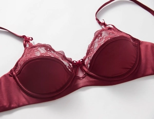 Detail view of burgundy satin bra with delicate lace trim and central bow accent