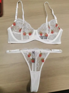 Detailed close-up of white mesh lingerie set with red strawberry embroidery and lace trim