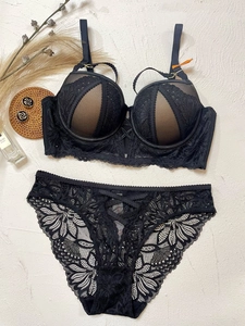 Flat lay of black lace lingerie set with underwire bra and floral panty on textured wall
