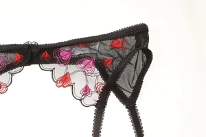 Detail of black lace garter with red heart embroidery and silk bow accent on white back