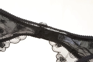 Detailed close-up of black lace thong with heart embroidery and a small satin bow