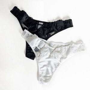 Detailed close-up of rose floral lace embroidery on black and white satin thong panties