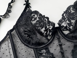 Detailed macro of black lace corset featuring floral embroidery and silk button accents