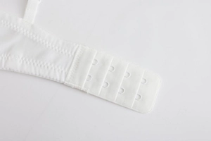 Detail of four-row back hook and eye closure on white seamless mesh bra with precise stitching