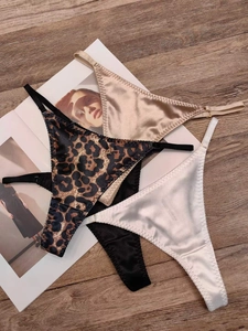 Detailed view of three satin thongs in leopard print and solid colors on a wood surface