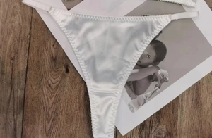 Detail of white satin thong with elastic straps on a wood texture background