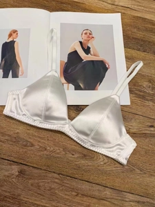 Detailed view of white satin triangle bralette with lace trim on dark wood background