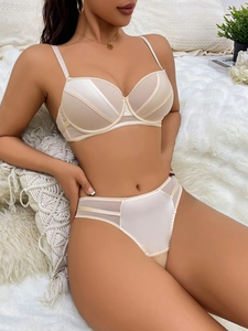 Detailed close-up of champagne lace lingerie set with mesh panels on white home background