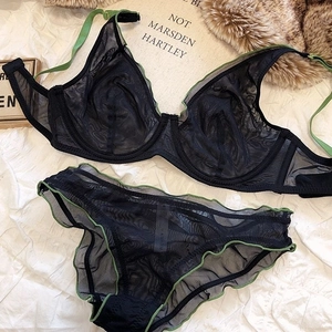 Black mesh lingerie set with green ruffle trim detail on a white fabric background