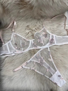 Detail of white mesh lingerie set with floral embroidery and underwire semi-cups on plush rug