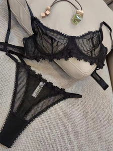 Detail of a black lace lingerie set with floral embroidery and tags on a light textured background