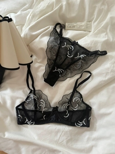 Detailed view of black sheer lace lingerie set with elegant white embroidery on bed