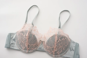 Detailed close-up of pink lace embroidery and light blue satin fabric on padded bra